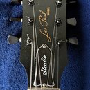 Černá hlava elektrické kytary s nápisy v zlatém provedení: Gibson, Les Paul MODEL a Studio. Na hlavě jsou vidět tři ladicí mechanismy z každé strany.…