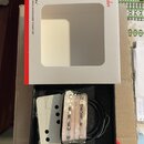 Bílá krabička s červeným pruhem a nápisy Fender, CUNIfe WIDE RANGE JAZZMASTER PICKUP SET. Uvnitř černé pěnové výplně jsou dva snímače zabalené v průh…