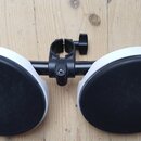 Dva kulaté černý padové bubny s bílým okrajem, které jsou upevněny na černé kovové hromádce. Celý mechanismus je umístěn na světlém dřevěném povrchu.…