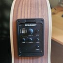 Detail na elektroniku akustické kytary s dřevěným povrchem. Černý ovládací panel nese nápis FISHMAN a označení Clásica III. Panel obsahuje otočný ovl…