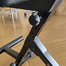 Detail černé kovové konstrukce hudebního stojanu nebo židle s černým polstrovaným sedákem. Na jedné z kovových nohou je bílý nápis frameworks. Konstr…
