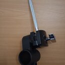 Černý kovový držák s kruhovým úchopem a stříbrným šroubem s knoflíkem. Z držáku vyčnívá stříbrný kovový hřebík s rýhovaným povrchem. Na černém plasto…