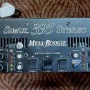 Černý kytarový zesilovač v rackovém provedení s úchyty po stranách. Na horním panelu je bílý nápis Simul. 395 STEREO a pod ním logo MESA/BOOGIE. Upro…