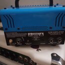 Modrý kompaktní kytarový zesilovač s černou rukojetí. Na zadním černém panelu je bílý nápis 20W AMPLIFIER, JOYO TECHNOLOGY CO., LTD a web www.joyoaud…