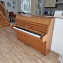 Dřevěný pianino v hnědém odstínu s viditnou strukturou dřeva. Nad klávesnicí je umístěn nápis „ZIMMERMANN“. Nástroj vykazuje známky běžného používání…