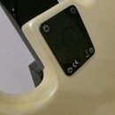 Detail zadní strany krémové elektrokytary s černým plastovým krytem elektroniky. Na krytu je vyrytý symbol lebky s překříženými kostmi a bílý nápis C…
