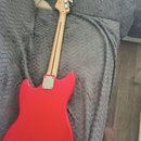 Zadní strana červené elektrické kytary s jasným lakem. Na hlavě je viditelné logo "Fender". Krk je vyroben ze světlého dřeva a na těle se nachází kov…