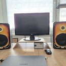Dva studiové monitory s dřevěným provedením v přechodové barvě od žluté po tmavě hnědou. Na spodní části každého reproduktoru je viditelné logo Gibso…