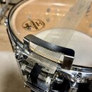 Detailní pohled na snare wire (sítko) u bubnu. Na horní membráně je viditelný nápis EVANS CALF CLASSIC RESONANT SNARE. Kovové mechanismy jsou chromov…