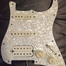 Bílý pickguard s perleťovým efektem osazený třemi snímači. Na dvou horních snímačích je nápis „R.M. pickups“, na spodním humbuckeru je částečně vidit…