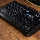 Černý digitální bubnový stroj s nápisy KORG a drumlogue HYBRID DRUM MACHINE. Zařízení obsahuje množství ovládacích knoflíků, malý displej s textem a…