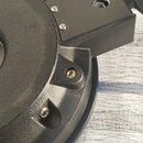 Detailní záběr na černý plastový nebo kovový komponent s texturovaným povrchem. Na součástce je viditelný nápis "OUTPUT" u jedné z konektorů. Povrch…
