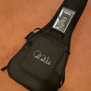 Černý poloměký obal na kytaru s přívěsným popruhem a úložnou kapsou. Na přední straně kapsy je bílý nápis Paul Reed Smith. Uvnitř obalu je vidět plas…