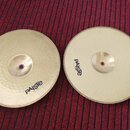 Dvě mosazné činely s vyvýšeným středem položené na červeném koberci. Oba mají černý nápis pAiste. Levý činel má povrch s viditelným kladivečkováním,…
