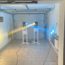 Dvě svítidla s modrým světlem umístěná na bílých stojaních v prostoru garáže. Na přední straně každého svítidla je bílý nápis "SoniX". Stojany mají k…