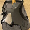 Zadní strana elektrické kytary v černé barvě, položená na šedém pouzdře. Na kovové krytce zadní části těla je vyryto logo „strandberg“. Povrch nástro…
