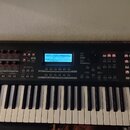Černý digitální syntezátor s klávesnicí. Na levé straně je bílý nápis YAMAHA a vpravo nápis MOXF6. Přístroj má centrální displej, několik posuvníků a…
