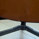 Detailní záběr na spodní hranu hnědého dřevěného nástroje, pravděpodobně kytary. Na černé hraně korpusu je viditelný malý odštípnutý kousek lakovanéh…