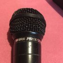 Černý dynamický mikrofon s kovovou síťkou. Na těle je nápis SHURE PROLOG. Povrch mikrofonu vykazuje drobné škrábance a opotřebení.