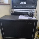 Na fotografii je černý kytarový kombozesilovač značky Harley Benton s bílým rámečkem kolem mřížky. Nad ním stojí černý zesilovač Laney s nápisem LET1…