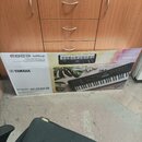 Fotografie zobrazuje kartónovou krabici s elektronickým klavírem. Na krabici je vidět logo YAMAHA a označení modelu PSR-E283. Povrch krabice vykazuje…
