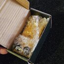 V otevřené kartonové krabici je v bublinkové fólii zabalený žlutý kytarový pedál. Na zařízení jsou vidět kovové ovládací prvky, ale žádné značky ani…
