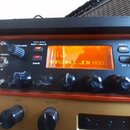 Detail kytarového zesilovače s oranžovým a zlatým panelem. Na displeji je nápis MARSHALL JCM 800 a nad ním nečitelné číslo. Na panelu jsou tlačítka E…
