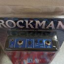 Modrý sluchátkový zesilovač v plastovém obalu. Na horní části obalu je velký bílý nápis ROCKMAN a pod ním text HEADPHONE AMPLIFIER & STEREO HEADSET.…