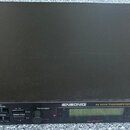 Černý rackový syntetizátor s nápisem ENSONIQ 64 Voice Expandable Synth. Na předním panelu jsou umístěny tlačítka, ovládací prvky a displej, v levém r…