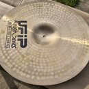 Kruhový činely z kovu s viditelným kladivováním po celé ploše. Na povrchu je černý nápis UFIP Rough Series EARCREATED CYMBALS a u středu malé číslo 1…