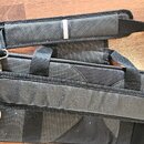Černý textilní obal na hudební nástroj s popruhem a rukojetí. Povrch je vyroben z odolného syntetického materiálu s viditelnou strukturou tkaniny. Na…