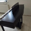 Černý digitální piano v provedení křídla s černými klávesami a bílými klavišmi. Na horní části je umístěn černý notový stojan. Na pravém boku korpusu…