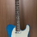 Modrá elektrická kytara typu Telecaster s bílým pickguardem a hnědým hmatníkem. Na hlavě krku je viditelné logo Fender. Nástroj vykazuje známky běžné…