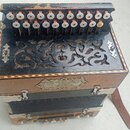 Černý harmonika s ozdobným dřevěným výřezem na přední straně a hnědými koženými popruhymi. Na předním panelu je viditelný štítek s nápisem „SOUBOR HU…