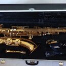 Zlatý saxofon v černém polstrovaném kufru. K nástroji je přiložen munčnípás s nápisem veti a samostatný mouthpiece. Na těle nástroje nejsou žádné čit…