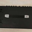 Zadní strana černého elektronického nástroje s rukojetí uprostřed. V horní části jsou vidět ovládací prvky a vlevo dvě ventilační mřížky. Na povrchu…