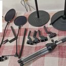 Sada černých mikrofonních stojanů a příslušenství rozložená na červenobílém ubrusu. Soubor obsahuje dva kulaté popfiltry, dvě základny stojanů a něko…