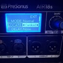 Detailní pohled na ovládací panel zařízení PreSonus AIR18s. Modrý podsvícený displej zobrazuje text: EXIT, MODE: Normal, LOCATE: Cardioid a DELAY: No…