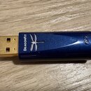 Modrý kovový USB dongle s pozlaceným konektorem. Na boku je bílý nápis DRAGONFLY a grafický symbol vážky. V zadní části je vyryté nečitelné označení.