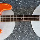 Oranžová elektrická basová kytara s červeným perleťovým pickguardem. Na hlavě hmatníku je nápis Vintage ICON Series. Povrch těla vykazuje výrazné odř…