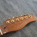 Detail hlavy elektrické kytary z hnědého dřeva se zlatými ladičkami. Na povrchu je bílý nápis Larry Carlton s malým symbolem vedle něj a na špičce hl…