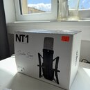 Bílá papírová krabice s produktovou fotografií černého mikrofonu v držáku. Na krabici jsou nápisy NT1, STUDIO CONDENSER MICROPHONE, Signature Series…