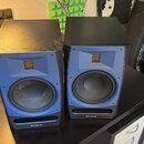 Dva studiové monitory v modré barvě s černými horními deskami a černým základním podstavcem. Na spodní části obou reproduktorů je bílý nápis PreSonus…