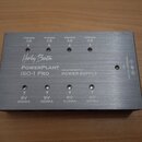 Stříbrný obdélníkový zdroj napájení z kovu s nápisy Harley Benton, PowerPlant ISO-1 Pro a ISOLATED OUTPUT POWER SUPPLY. Na horní straně jsou čtyři vý…