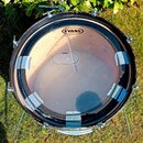 Fotografie znázorňuje basový buben s průhlednou blanou. Na blaně je nápis EVANS GAMUT a menší logo EVANS s textem MADE IN USA. Okraj blány je přilepe…