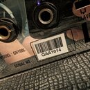 Detail zadní strany zesilovače s černým povrchem a dvěma konektory. Na povrchu je nápis MODEL : GH100L a vedle něj náleplka s čárovým kódem a označen…