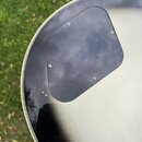 Detail zadní strany kytary v černé barvě. Na povrchu je přišroubovaný černý plastový kryt elektroniky s rounded rohy. Lak v okolí krytu vykazuje drob…