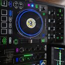 Černý DJ kontrolér značky DENON DJ s podsvícenými tlačítky a modře podsvíceným jog-wheel. Uprostřed jog-wheelu je žlutý kulatý štítek s obrázkem post…