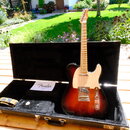 Elektrická kytara s tmeleým sunburst povrchem těla a světlým hmatníkem z javoru. Nástroj má bílý pickguard a na hlavě je viditelné logo Fender. Kytar…
