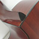 Detail zadní strany akustické kytary v místě spoje krku s tělem. Nástroj má tmavě hnědý lakovaný povrch. V místě spoje jsou viditelné škrábance a opo…